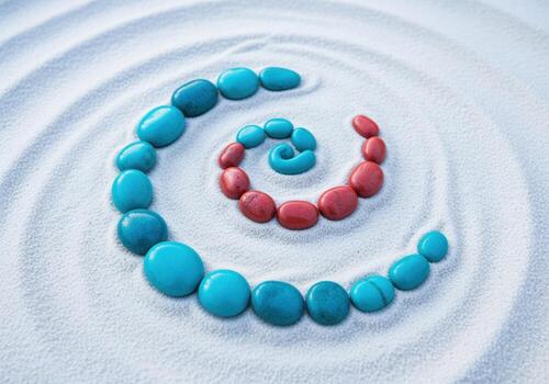 Smooth turquoise and coral red river stones arranged in a perfect spiral pattern on fine white sand photo