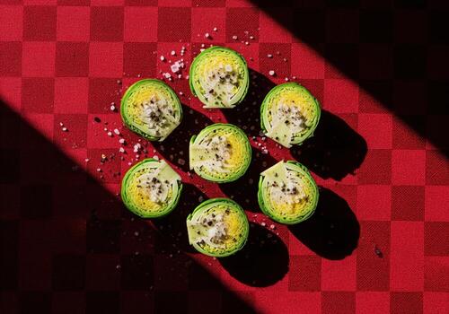Bright green brussels sprouts cut in half, seasoned, arranged on a red checkered tablecloth with harsh light photo