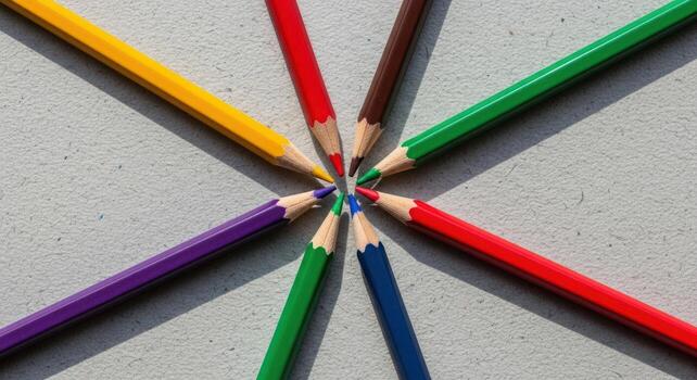 Vibrant sharpened colored pencils arranged in a radial pattern on a light grey surface photo