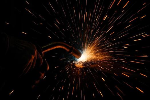 Close up of intense welding arc and explosive sparks from a torch in a dark industrial setting photo