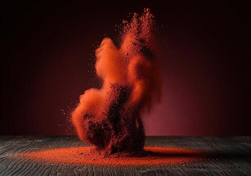 Turbulent burst of vibrant red ochre powder exploding upwards from a dark wooden surface. photo