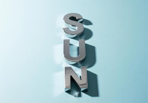 Bright minimalist flat lay with polished chrome letters spelling SUN on blue surface photo