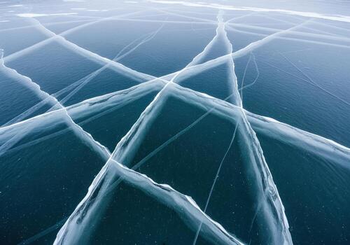 Geometric cracks on clear blue ice covering a deep winter lake surface photo