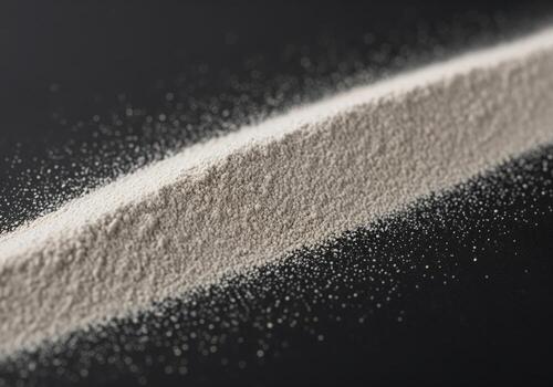 Scattered line of fine light grey powder material on a dark surface photo