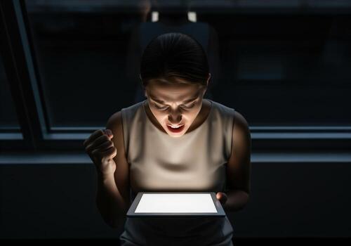 Dramatic woman illuminated by tablet screen expressing intense emotion and success photo