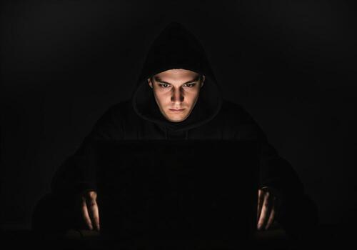 Young man in hoodie focused on screen in dark, intense hacking or coding photo
