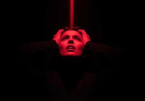 Distressed woman in red light, hands on head, expressing fear and pain photo