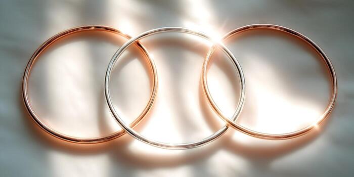 Three shiny metallic rings one silver and two rose gold interlock creating a symbolic connection on a soft illuminated surface photo
