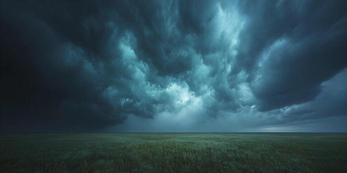 Dark heavy storm clouds gather dramatically over a wide open green field creating an ominous and powerful natural scene photo