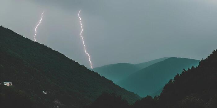 Bright lightning strikes multiple times in a dramatic mountain range during an intense thunderstorm photo