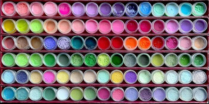 An overhead view of numerous small clear jars filled with vibrant colorful powders and gels neatly displayed in rows on shelves photo