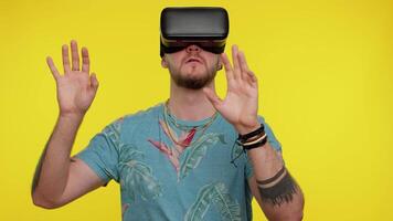 förvånad turist vuxen man använder sig av headsetet hjälm app till spela simulering spel. tittar på virtuell verklighet 3d 360 . ung kille i vr glasögon isolerat på gul bakgrund. missbruk från teknologi video