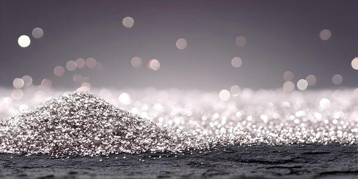 A shimmering pile of silver glitter sits on a dark textured surface with sparkling bokeh lights in the background photo