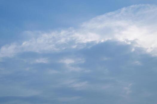 A view of a partly cloudy sky with sunbeams piercing through. Dark clouds sit at the bottom left, contrasting with the brighter, scattered clouds and the clear blue sky. photo