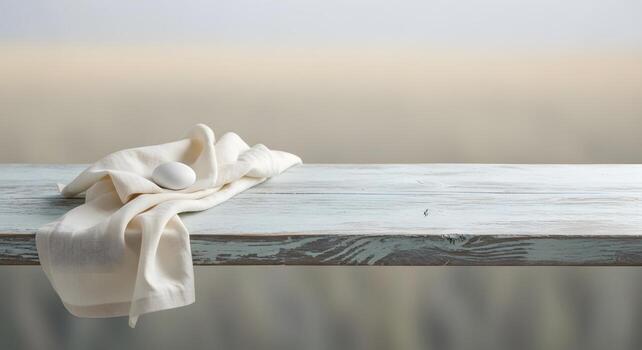 A single white egg rests on a soft, draped linen cloth atop a weathered, rustic wooden table with a blurred, neutral background photo
