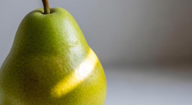 Close up of a single green pear with sunlight casting a shadow across its surface, highlighting its texture and smooth skin against a blurred background photo
