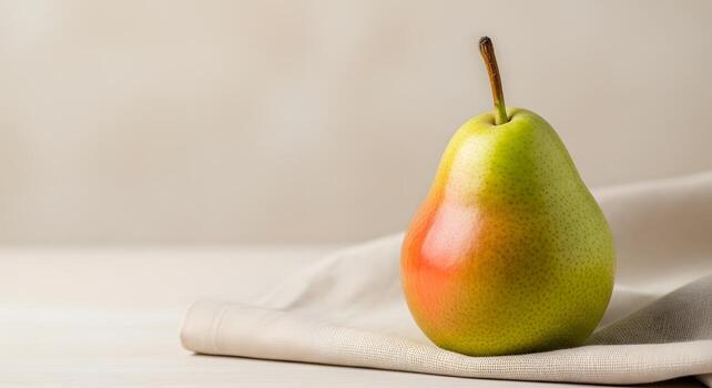 A single ripe pear with a blend of green and red hues sits on a folded white cloth with a soft, neutral background photo