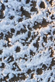 Delgado capa de nieve en desnudo tierra a puesta de sol con natural patrones y suave ligero oscuridad. foto