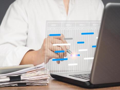 Close-up of project manager working on a laptop and updating tasks and milestones progress planning with a Gantt chart scheduling interface on a virtual screen. photo