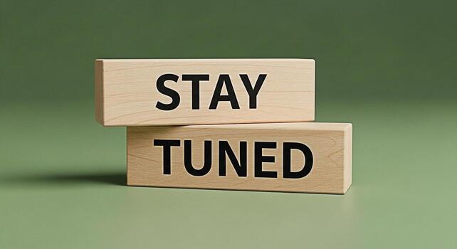 Wooden blocks stacked on a green surface displaying the message Stay Tuned in bold black letters creating anticipation and excitement for upcoming news or announcements in a minimalist setting photo