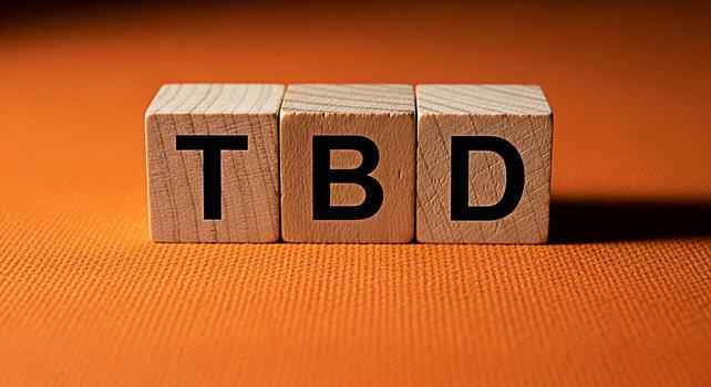 Wooden blocks displaying TBD on a textured orange surface representing an uncertain future and awaiting confirmation symbolizing anticipation and the need for planning in a vibrant and dynamic setting photo