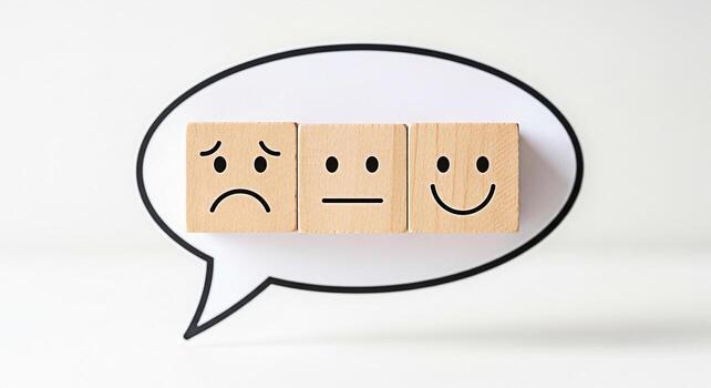Wooden blocks displaying different facial expressions inside a speech bubble on a white surface representing customer feedback emotional spectrum and the importance of understanding and responding to photo