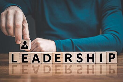 A person adding a block with a leader icon to wooden blocks spelling LEADERSHIP on a wooden table symbolizing building strong leadership and management skills for success in business and career growth photo