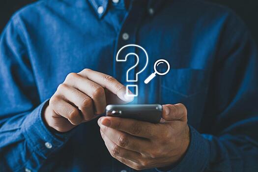 Man in a blue shirt using a smartphone with a glowing question mark and magnifying glass overlay symbolizing problemsolving and information seeking in a digital age conveying curiosity and innovation photo