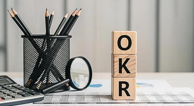 Wooden blocks spelling OKR on a desk with pencils calculator and magnifying glass representing Objectives and Key Results in a business setting conveying a sense of focus planning and strategic goal s photo