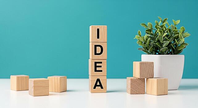 Wooden blocks spelling IDEA stand tall on a white table against a teal background symbolizing creativity and innovation with a small potted plant adding a touch of nature and freshness to the scene photo