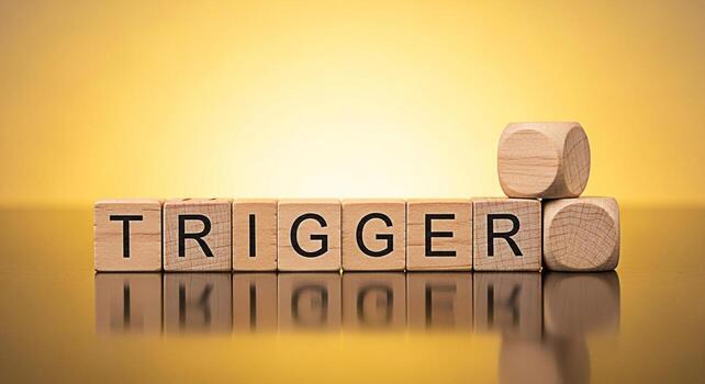 Wooden blocks spelling TRIGGER on a reflective surface against a golden gradient background representing a sensitive topic a catalyst for change or a psychological stimulus evoking feelings of awarene photo