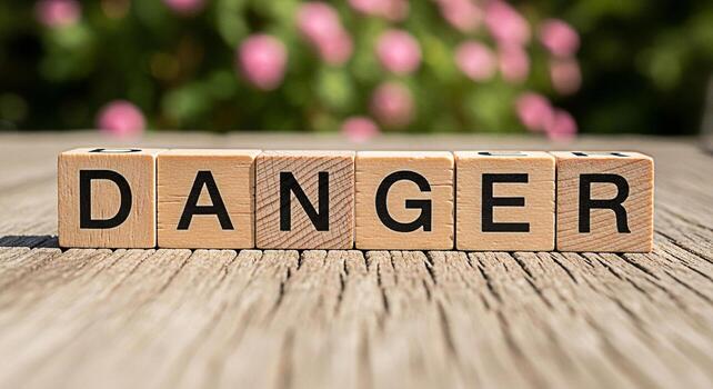 Wooden blocks spelling DANGER resting on a weathered wooden surface in a garden setting conveying a sense of caution and awareness about potential hazards in a natural environment photo