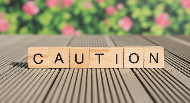 de madera bloques ortografía precaución en un de madera superficie en contra un borroso floral antecedentes transporte un mensaje de advertencia y la seguridad conciencia en un natural y sereno ajuste enfatizando el importancia de foto