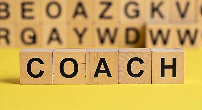 Wooden blocks spelling COACH on a bright yellow surface symbolizing guidance and mentorship in a learning environment fostering a positive and supportive atmosphere for personal and professional devel photo