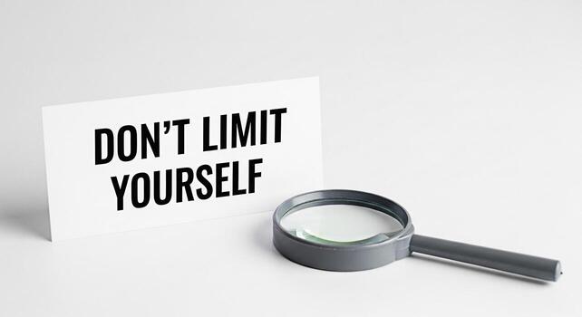 A motivational message Dont Limit Yourself displayed on a white card next to a magnifying glass on a clean white surface symbolizing selfimprovement potential and the power of positive thinking in a m photo