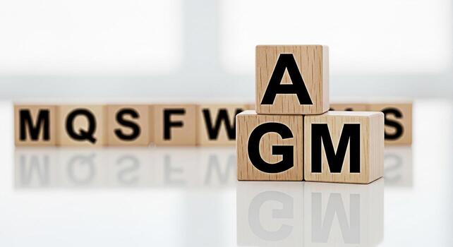 Wooden blocks spelling out AGM stacked on a reflective white surface with other blocks displaying random letters in the background conveying a sense of business meetings and corporate governance in a photo