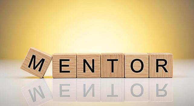 Wooden blocks spelling MENTOR arranged on a reflective surface against a gradient yellow background symbolizing guidance support and the importance of mentorship in personal and professional developme photo