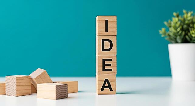 Stack of wooden blocks spelling IDEA on a white table against a teal background symbolizing creativity innovation and the generation of new concepts in a bright and inspiring workspace environment photo