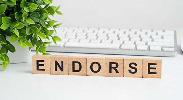 Wooden blocks spelling ENDORSE on a white desk next to a green plant and a computer keyboard representing a positive review support and agreement in a clean and modern office environment photo