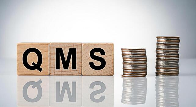 Wooden blocks displaying QMS next to stacks of coins on a reflective surface symbolizing quality management systems and financial growth representing business success and strategic planning in a corpo photo