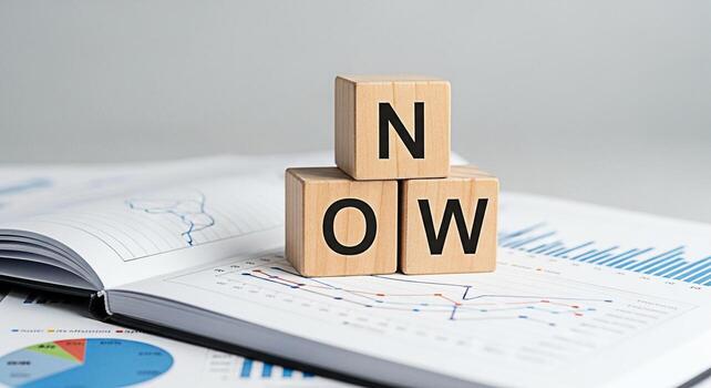 Wooden blocks spelling NOW resting on an open notebook filled with financial charts and graphs symbolizing immediate action and decisionmaking in a business environment fostering a sense of urgency an photo