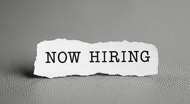 Torn paper piece displaying the message Now Hiring on a textured gray background symbolizing job opportunities and recruitment efforts creating a sense of urgency and new beginnings for potential cand photo