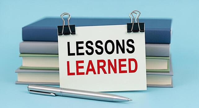 A stack of books on a blue surface featuring a note card with the words Lessons Learned in bold black and red letters conveying a message of education experience and personal growth in an academic set photo