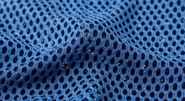 Close-up view of a vibrant blue mesh fabric texture with a pattern of hexagonal holes and water droplets, showcasing detail and design photo