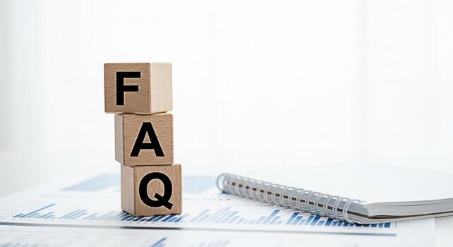 Wooden blocks displaying FAQ on a bright white desk with financial charts and a notebook representing frequently asked questions and information resources for business and customer support photo