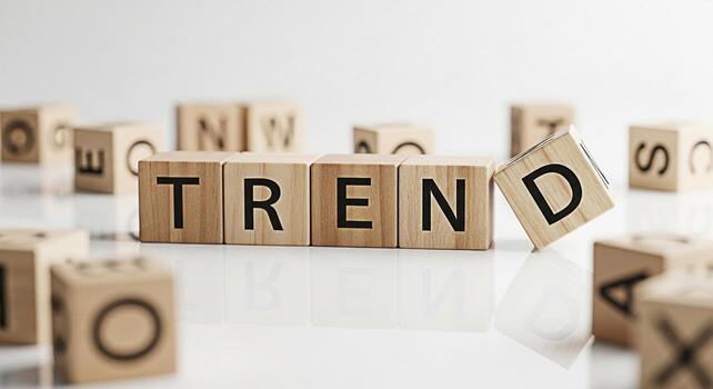 Wooden blocks spelling TREND on a reflective white surface with scattered letter blocks representing emerging patterns and popular topics in a clean minimalist environment conveying a sense of modern photo