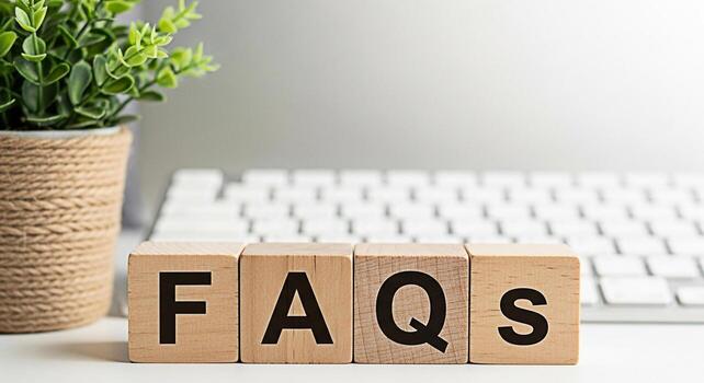 Wooden blocks spelling FAQs on a white desk with a keyboard and a potted plant representing information accessibility and customer support in a clean and modern office environment conveying a sense of photo