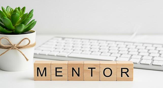 Wooden blocks spelling MENTOR on a white desk next to a potted succulent and keyboard representing guidance support and professional development in a clean and modern office environment fostering a po photo