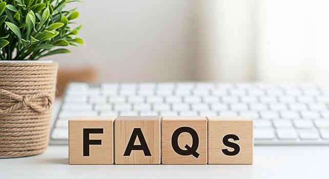 Wooden blocks spelling FAQs on a white desk with a blurred keyboard and a potted plant representing frequently asked questions and information access in a modern and minimalist office setting photo