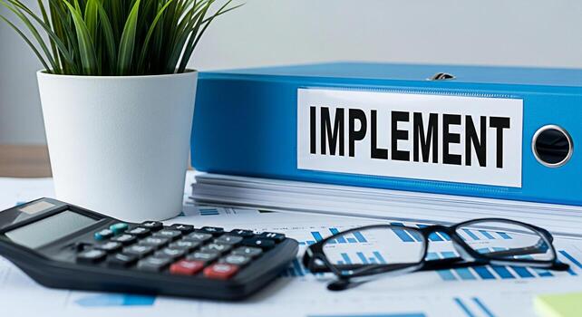 Closeup of a blue binder labeled IMPLEMENT on a desk with a calculator glasses and financial charts symbolizing project implementation and the importance of meticulous planning in a business setting photo